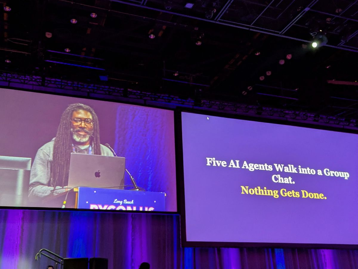 Lawrence Gray at the lectern at PyCon US 2026 beside a slide reading Five AI Agents Walk into a Group Chat. Nothing Gets Done.